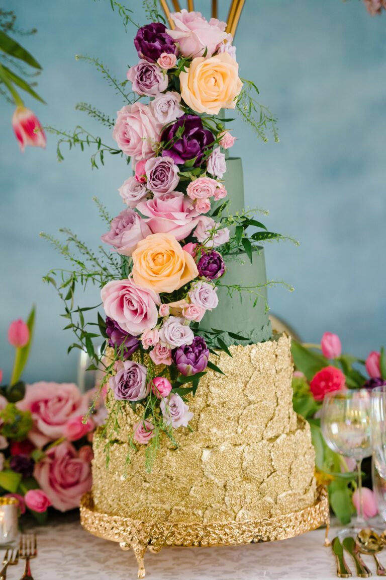A tiered cake with a cascade of sugar roses in pink, orange and purple above gold leaf texture, Tees Bakery