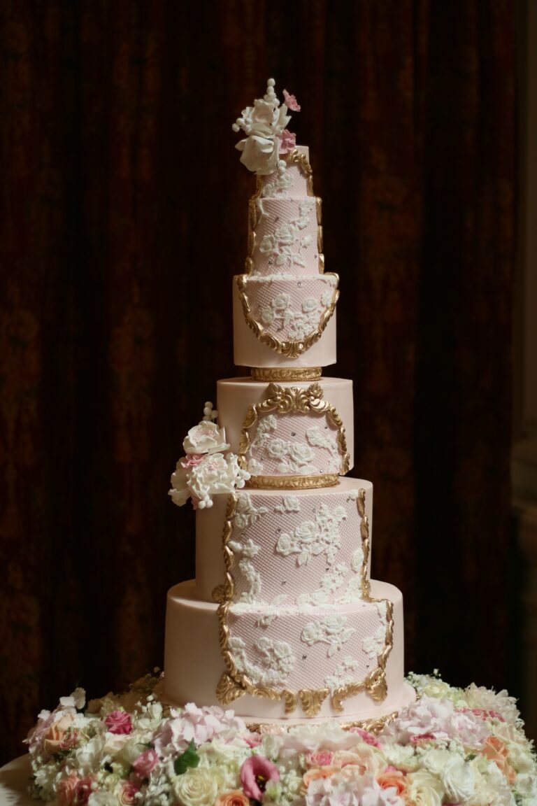 A cream tiered cake with gold relief moulding and a floral base, Tees Bakery