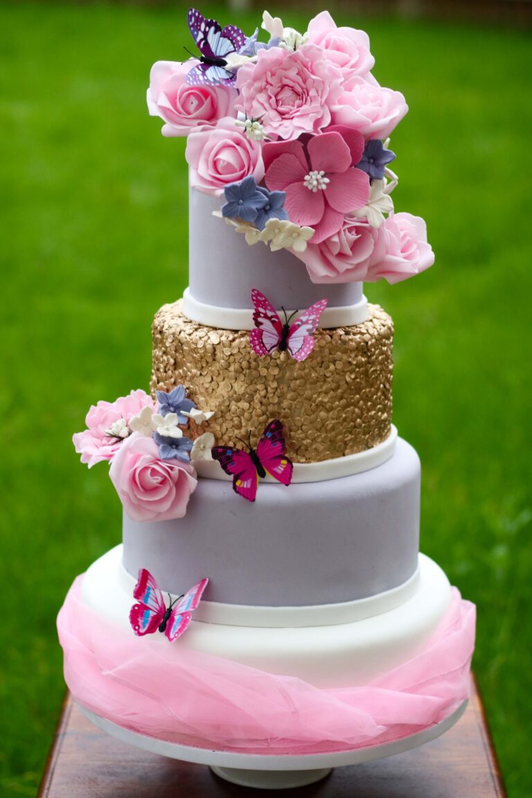 A grey, gold sequin and pink cake with sugar roses and butterflies on a lawn, Tees Bakery