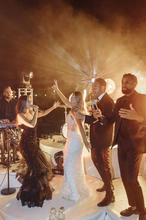 A bride and groom with a band and guests on a lit dance floor at night