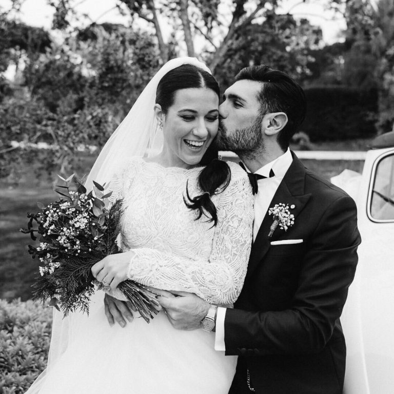 A black-and-white portrait of a bride and groom embracing in a garden