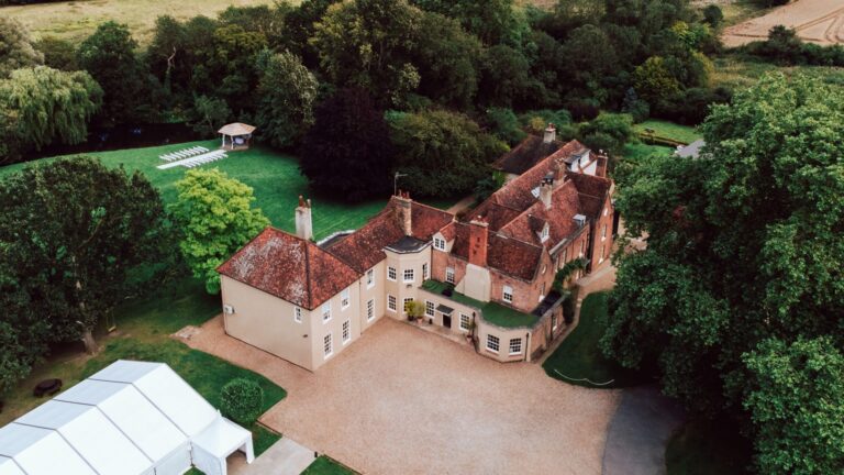 Aerial view of the house, the white marquee beside it, the lawns and the lakeside gazebo among mature trees, That Amazing Place