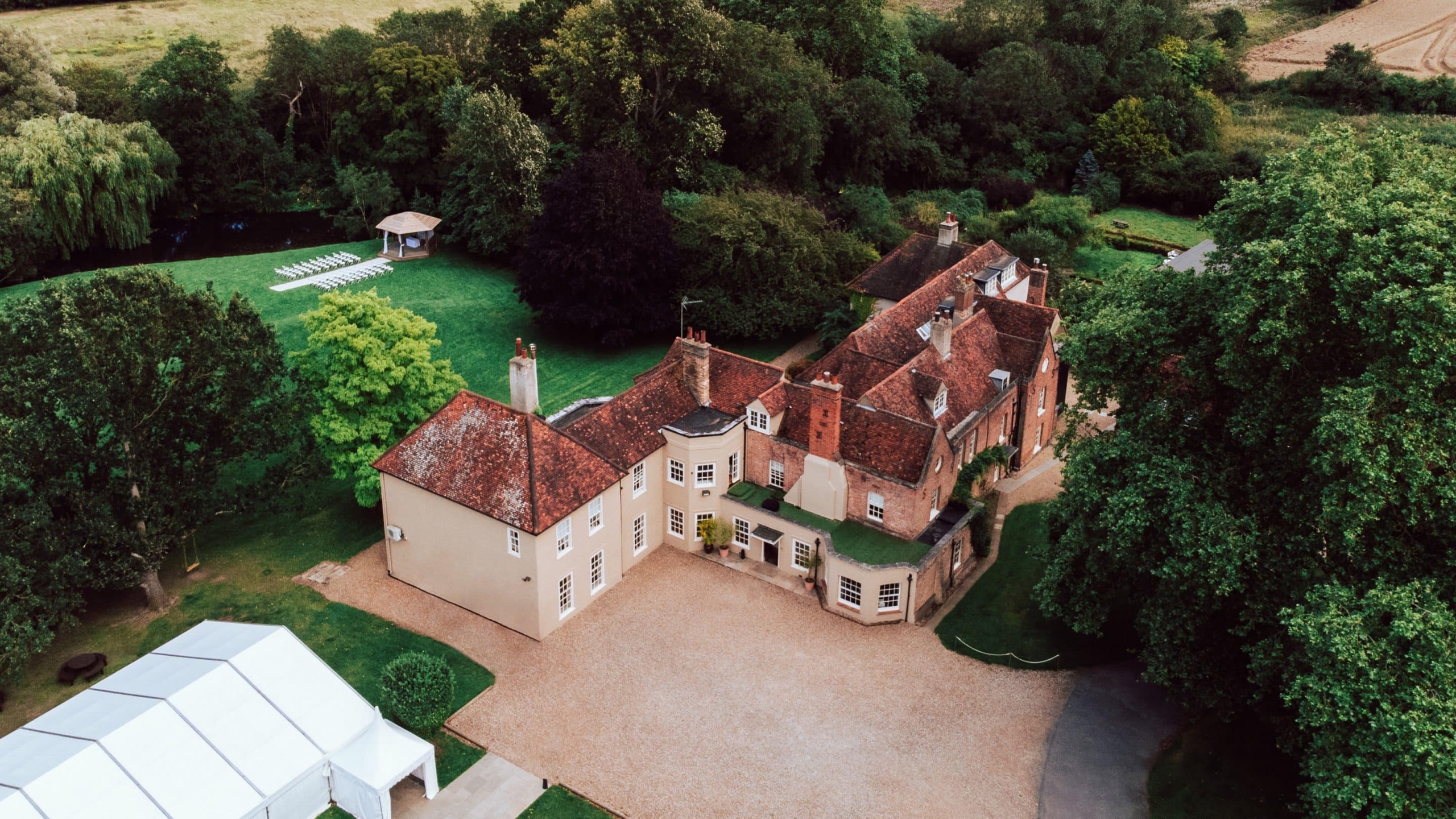 Aerial view of the house, the white marquee beside it, the lawns and the lakeside gazebo among mature trees, That Amazing Place