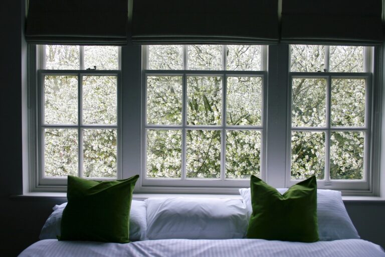 A guest bedroom bed beneath a wide sash window looking onto blossom, That Amazing Place