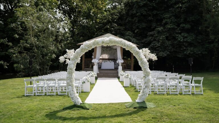 An outdoor ceremony on the lawn with a white aisle runner and a floral arch leading to the gazebo, That Amazing Place