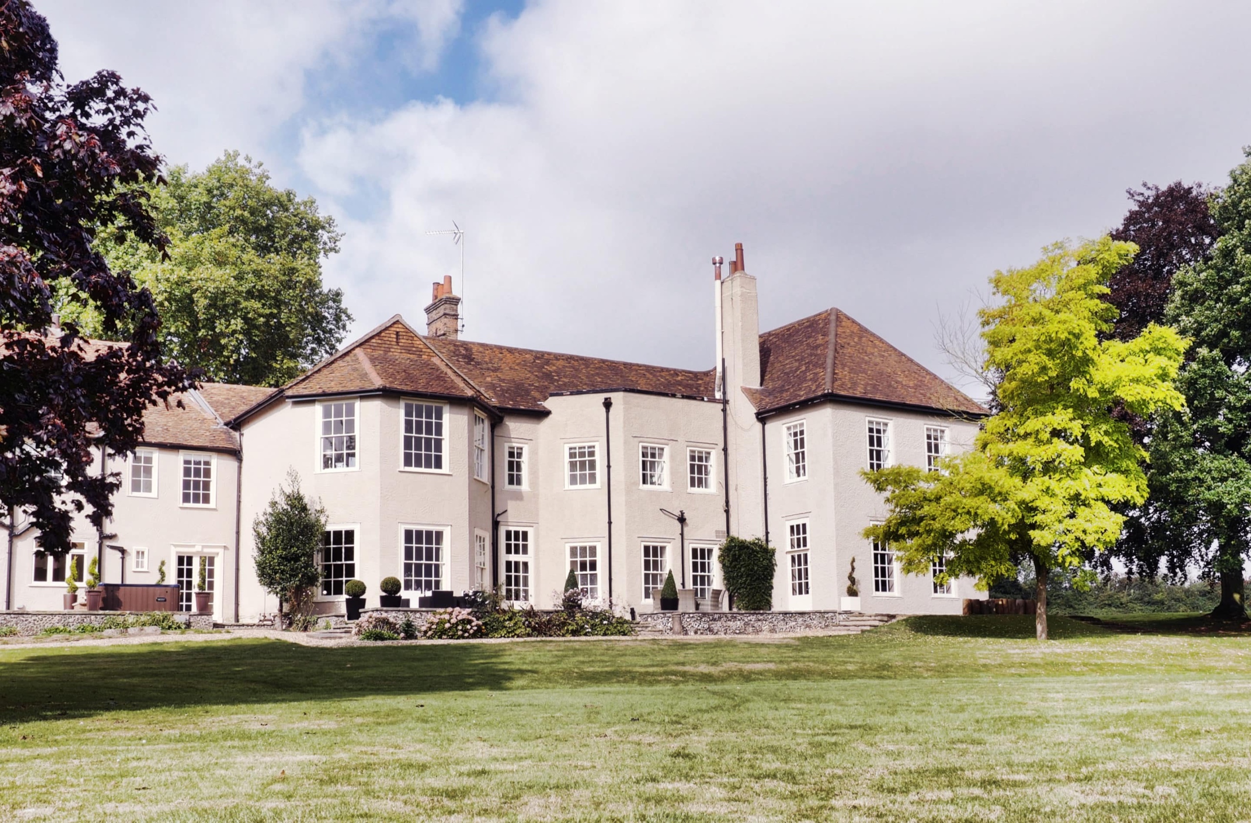 The rendered rear elevation with its bay windows, seen across the lawn under a blue sky, That Amazing Place