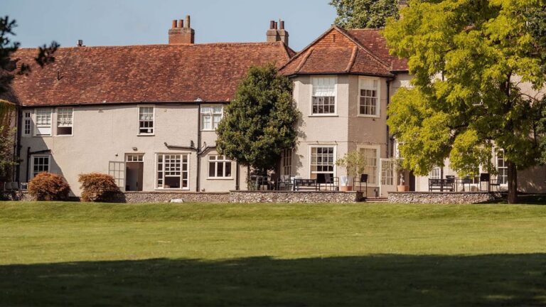 The long rear range of the house with sash windows and red tiled roofs above a wide lawn, That Amazing Place