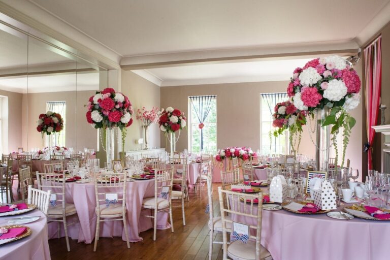 The Hall dressed for a wedding breakfast with round tables, pink linen and tall flower arrangements, That Amazing Place