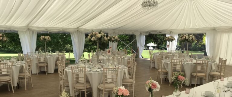The marquee with its panoramic side walls opened onto the grounds, tables laid for dinner, That Amazing Place