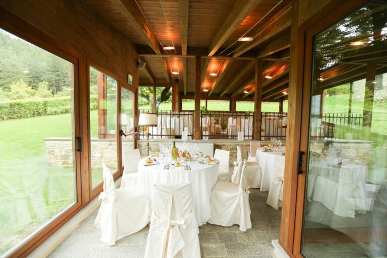 The glazed loggia, white-clothed tables under a timber ceiling above the valley, The Abbazia San Faustino