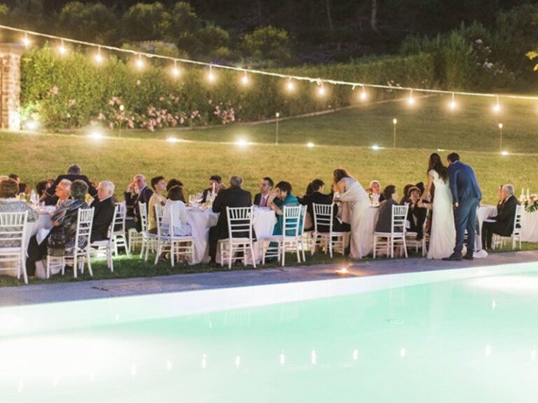 Dinner by the pool under festoon lights, a long table at dusk, The Abbazia San Faustino