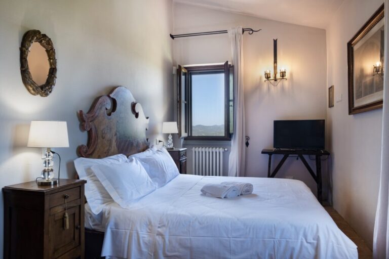 A bedroom with antique nightstands, white linen and a gilt mirror, The Abbazia San Faustino