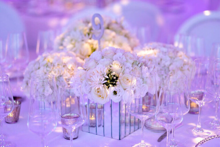 White floral centrepieces in mirrored holders under violet lighting, The Admirable Crichton