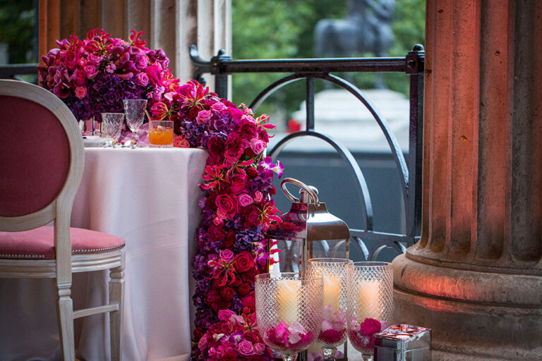 Pink and magenta floral arrangement with candles beside a stone column, The Admirable Crichton