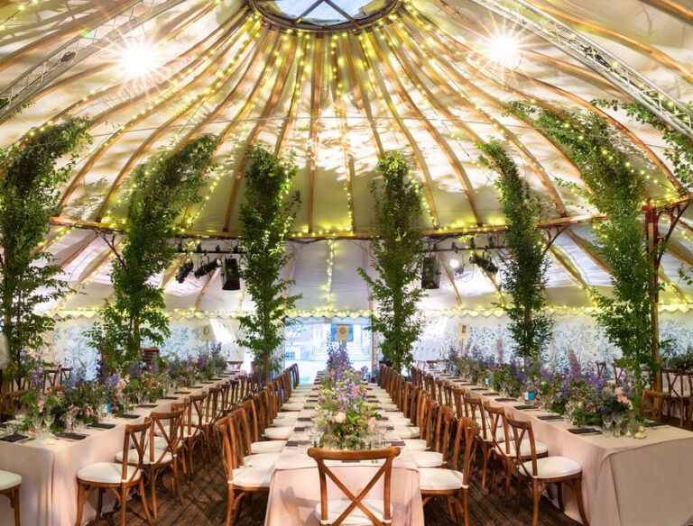 Pavilion marquee with greenery-wrapped poles and long banqueting tables, The Admirable Crichton