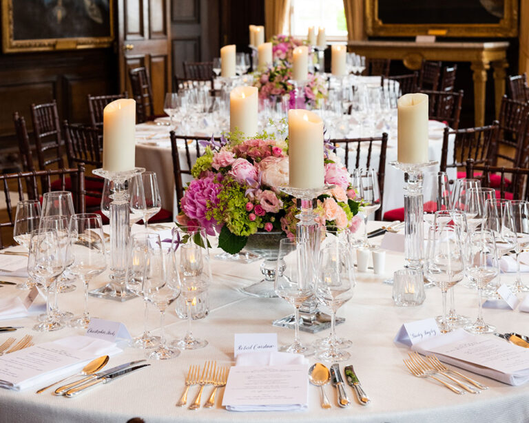 Candlelit round table with pink and white flowers in an oak-panelled room, The Admirable Crichton
