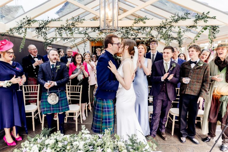 The ceremony kiss before guests beneath a floral arch in the Conservatory, The Bay Tree Hotel