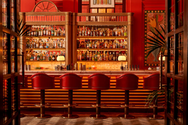 The marble bar and red leather stools of The Coral Room, with its back bar lit in gold, The Bloomsbury