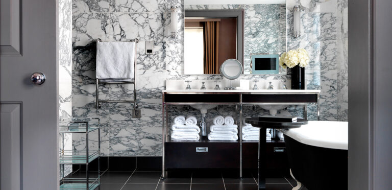 A marble bathroom with a double vanity, towel shelves and a roll-top bath, The Bloomsbury
