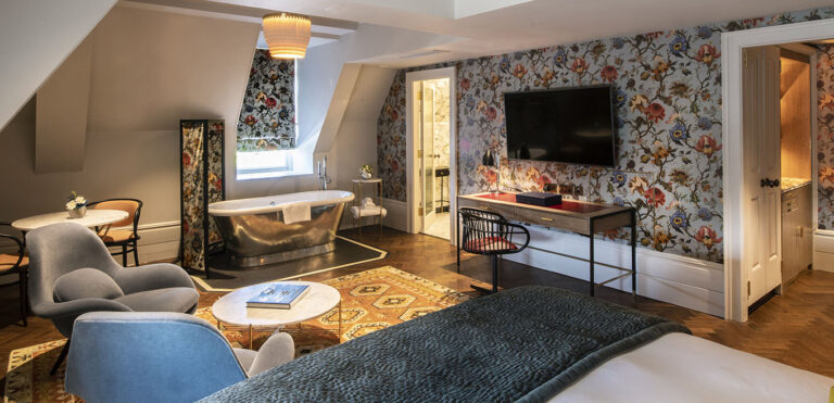 A Luxury Studio Suite under the eaves, with a freestanding metal bath in the room, floral wallpaper and parquet floor, The Bloomsbury