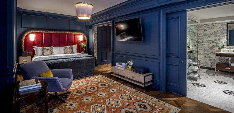 A Studio Suite with navy panelled walls, a red leather headboard and a marble bathroom through the open door, The Bloomsbury