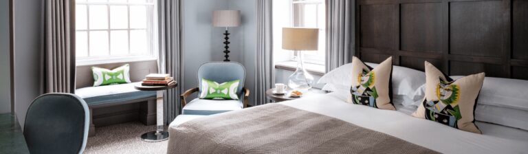 A Deluxe King room with a dark panelled headboard, window seat and armchair, The Bloomsbury