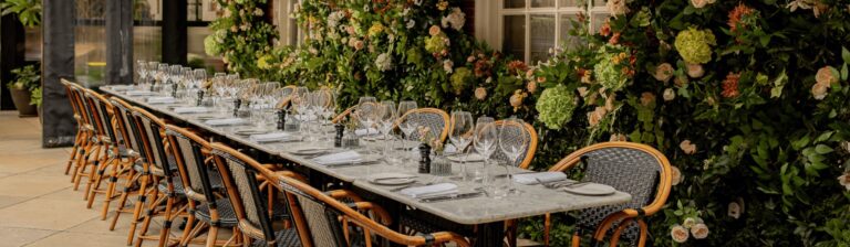 A long table on Dalloway Terrace laid for a private dinner, framed by flowering walls, The Bloomsbury