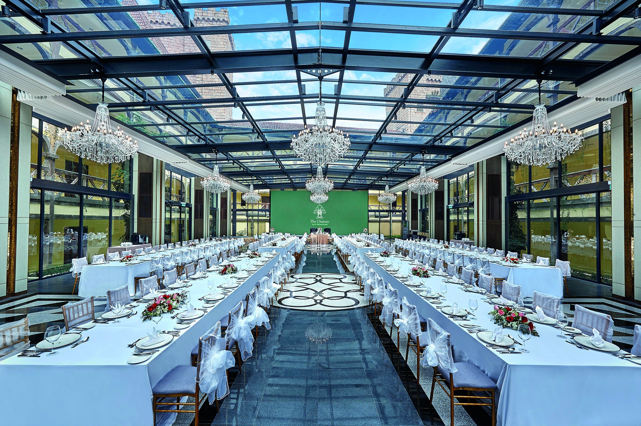 Reception tables set beneath chandeliers in the glass-roofed hall, The Chateau Spa and Organic Wellness Resort