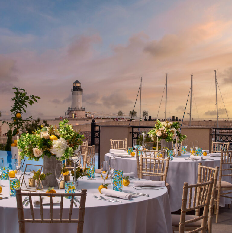 Round tables laid for dinner at sunset with the lighthouse in view, The Chedi Luštica Bay