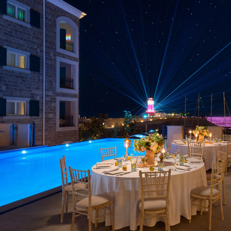 A round table laid for dinner beside the pool after dark, The Chedi Luštica Bay
