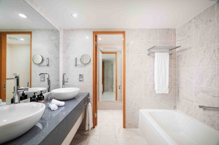 A refurbished suite bathroom in pale marble with twin basins and a bath, The Chelsea Harbour Hotel