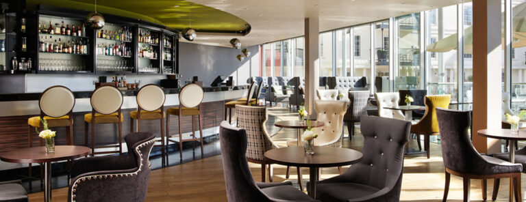 The hotel bar with high stools and buttoned armchairs beside full-height windows onto the harbour, The Chelsea Harbour Hotel