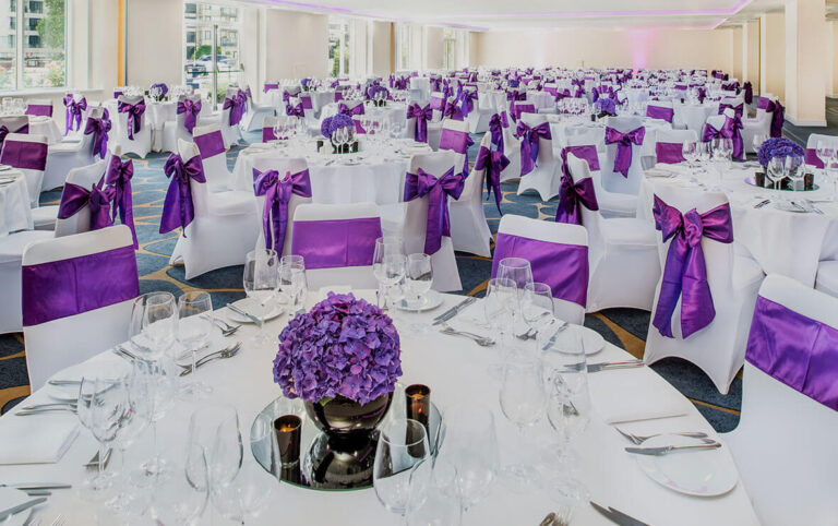 The Grand Room set for a large banquet, white chair covers tied with purple sashes and hydrangea centrepieces, The Chelsea Harbour Hotel