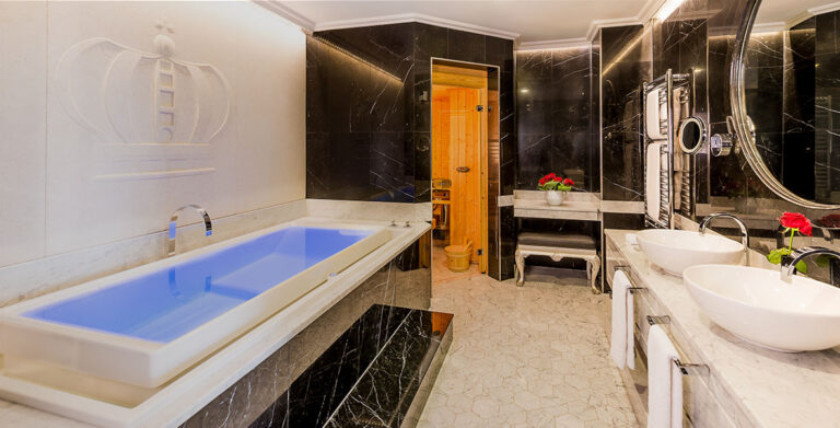 The in-room spa bathroom of the Kings Penthouse Suite, with a lit bath, sauna door and twin basins, The Chelsea Harbour Hotel