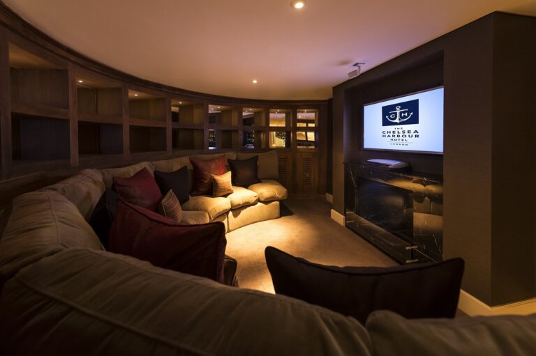 The home cinema room in The Savile Penthouse, a curved sofa facing the screen, The Chelsea Harbour Hotel