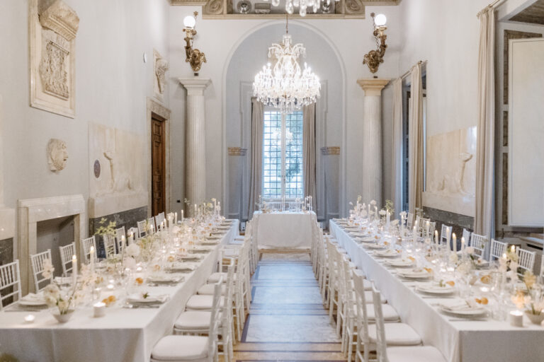 A frescoed palazzo hall laid with long white tables beneath a chandelier, The Dream Wedding Lab