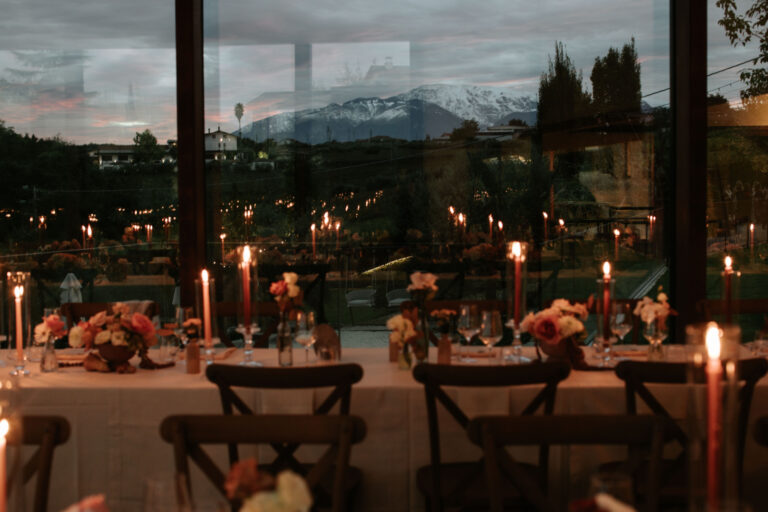 Candlelit reception tables beside tall windows with a mountain view at dusk, The Dream Wedding Lab