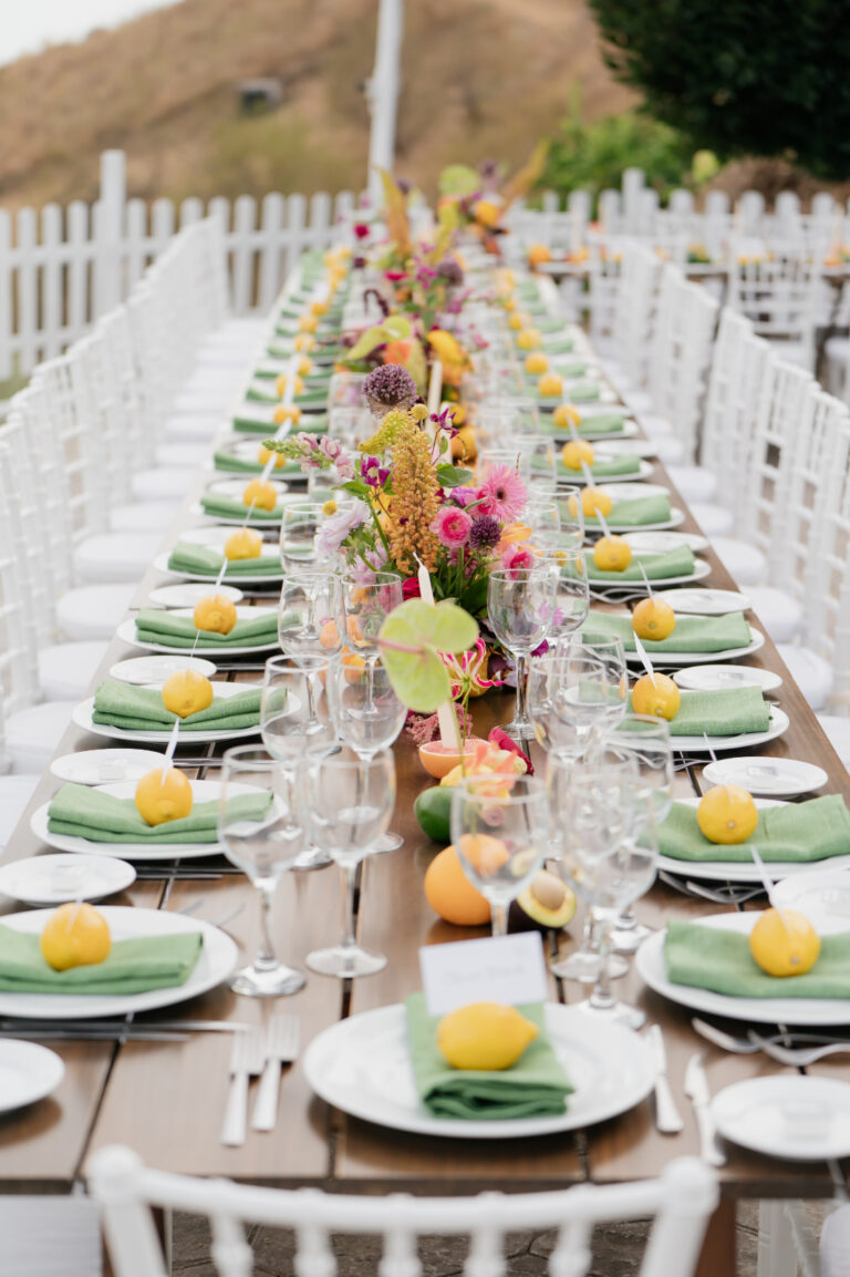A long white-chaired table set with lemons, green napkins and bright flowers, The Dream Wedding Lab
