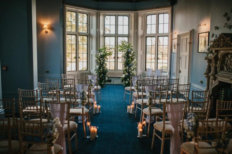 A ceremony room with a deep bay window, blue carpet and dressed chiavari chairs, The Elvetham