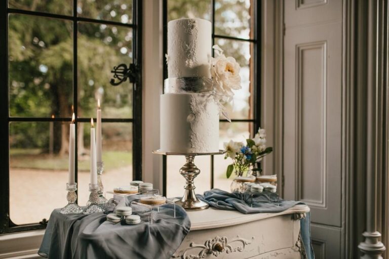 A tiered wedding cake by tall windows on a styled table, The Elvetham