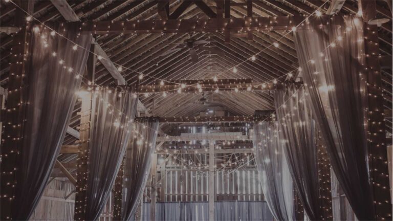 A barn hung with drapes and fairy lights for a reception, The Event Studio