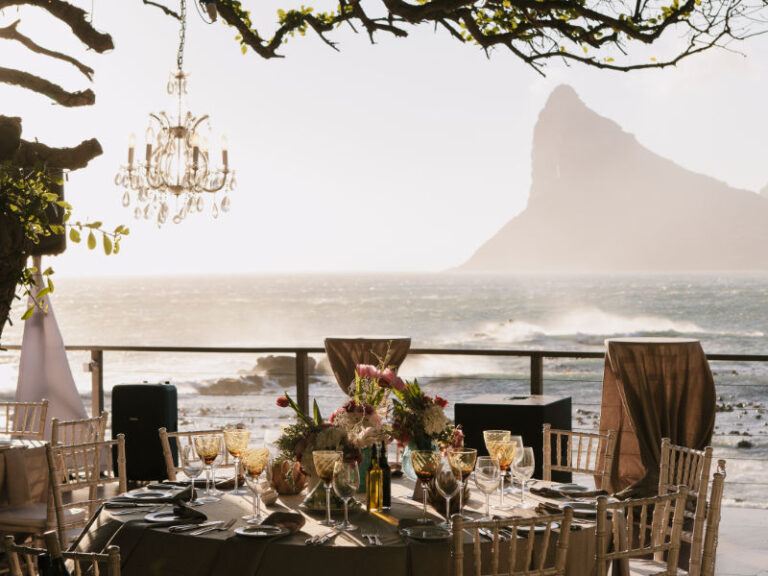 A table dressed under a chandelier on a terrace above the sea, with mountains beyond, The Event Studio