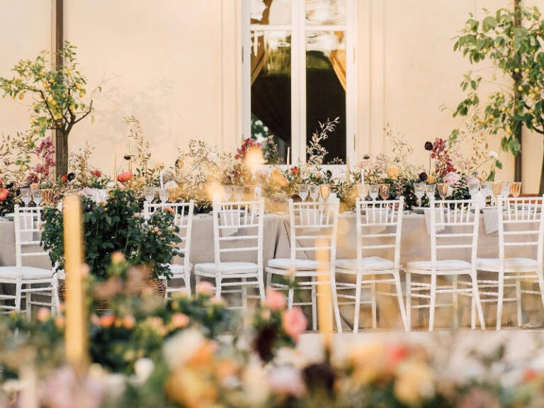Long banquet table with white chairs and abundant garden flowers in a glasshouse setting, The Event Studio