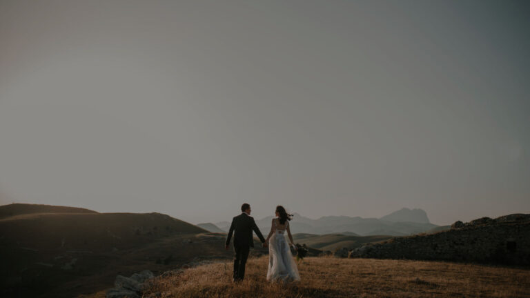 Bride and groom walking hand in hand across open hills at dusk, The Event Studio