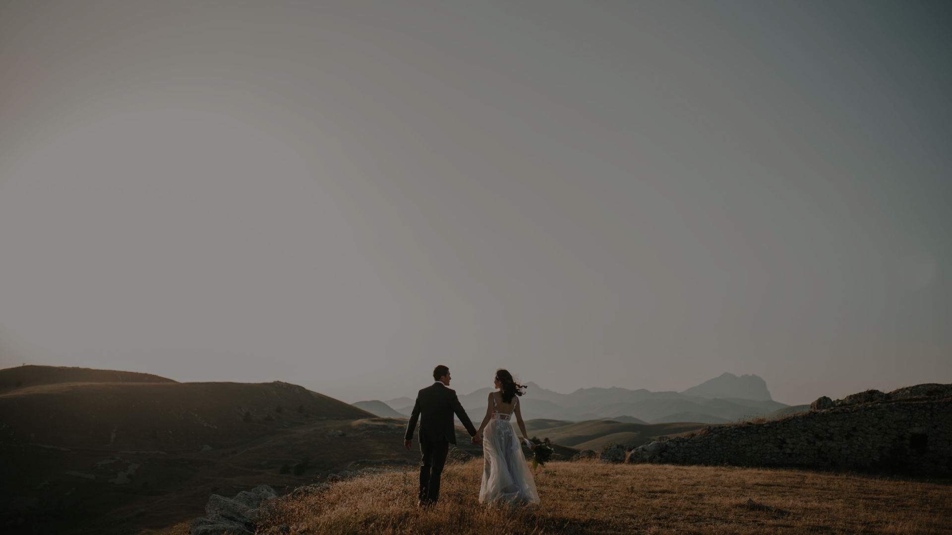 Bride and groom walking hand in hand across open hills at dusk, The Event Studio