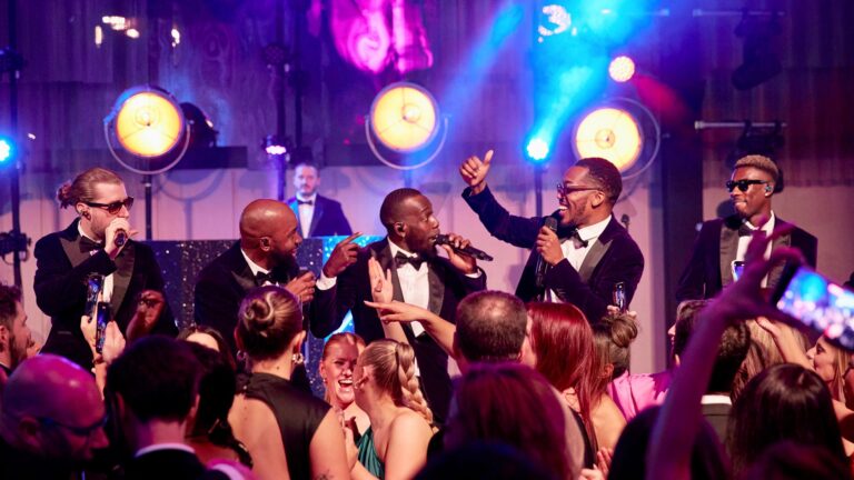 Vocalists on stage with guests dancing in front, warm stage lamps behind, The Function Band