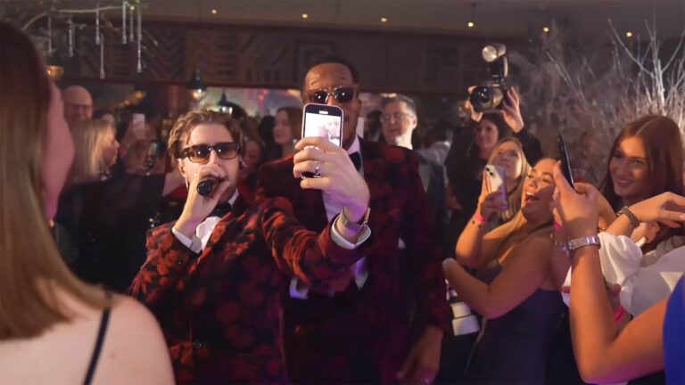 Singer in a red patterned jacket filming a selfie with guests at an evening party, The Function Band