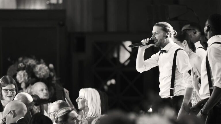 Black and white image of a vocalist singing among wedding guests, The Function Band