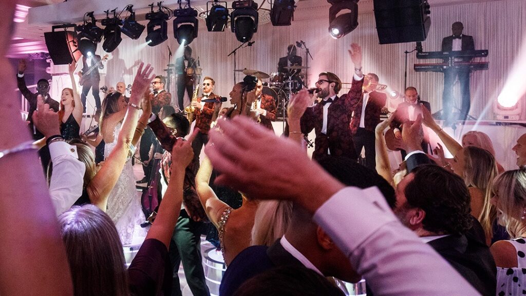 Band on stage as guests dance with raised arms under stage lighting, The Function Band