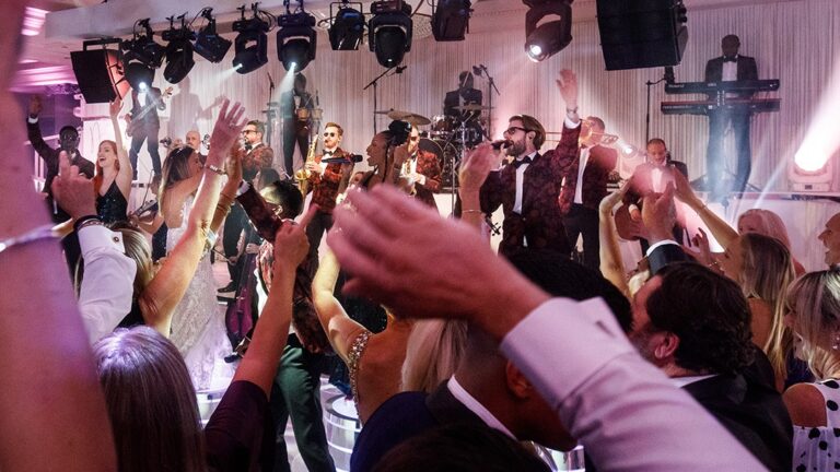 Band on stage as guests dance with raised arms under stage lighting, The Function Band